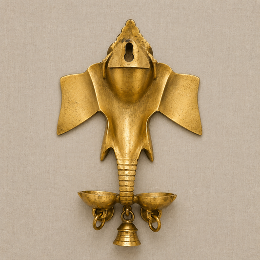 An ornate brass Ganesha hanging oil lamp with colorful stone work details and three hanging bells, set against a solid beige background.