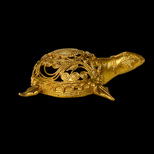 An ornate gold Dokra turtle figurine with intricate filigree detailing on its shell, shown against a solid black background.