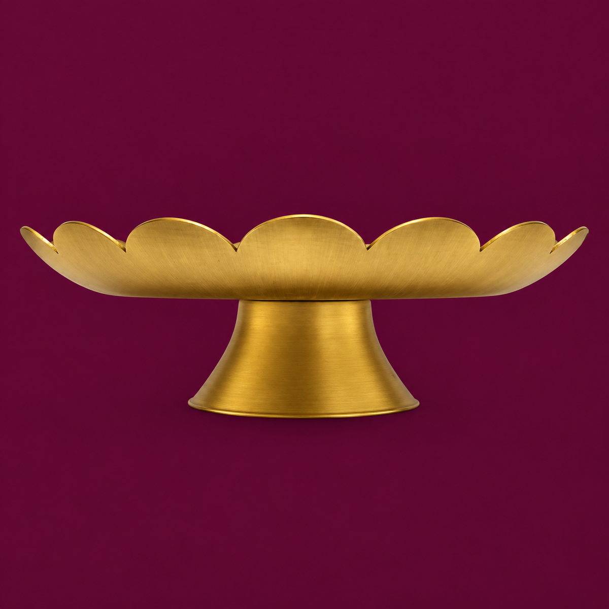 A golden brass cake stand stand with a scalloped rim, shown against a solid deep magenta background.