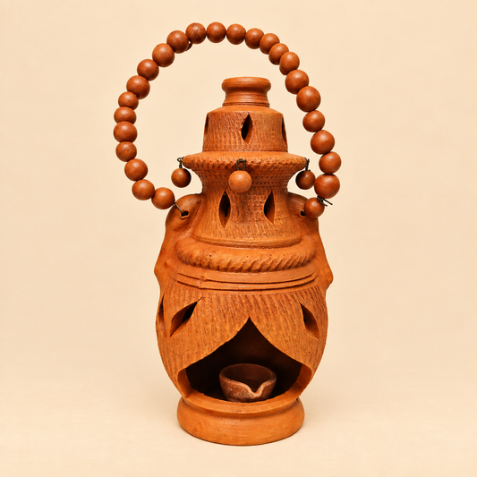 A hand-carved terracotta oil lamp with a decorative beaded handle, shown against a solid beige background.