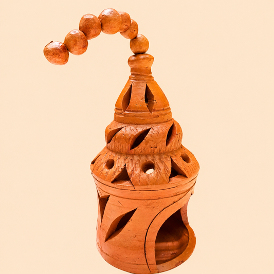 An orange-brown terracotta hanging lamp with carved cutouts and a beaded hanging loop, shown against a solid pale peach background.