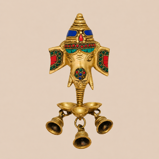 An ornate brass Ganesha hanging oil lamp with colorful stone work details and three hanging bells, set against a solid beige background.