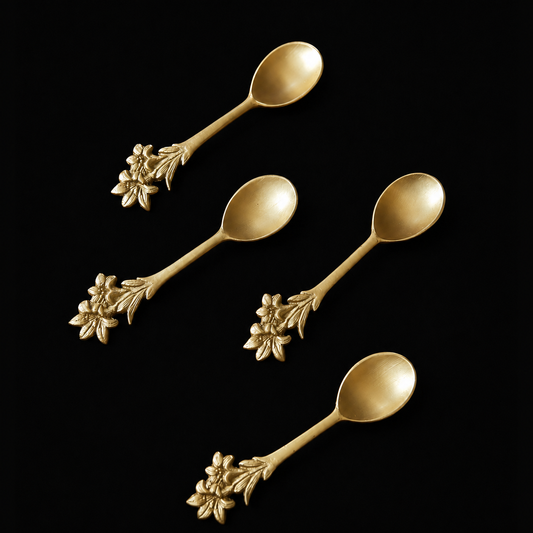 Four golden brass spoons with ornate floral handles, arranged diagonally on a solid black background.