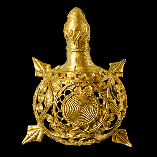 An ornate gold-toned Dokra turtle figurine with intricate filigree and spiral detailing, photographed against a solid black background.