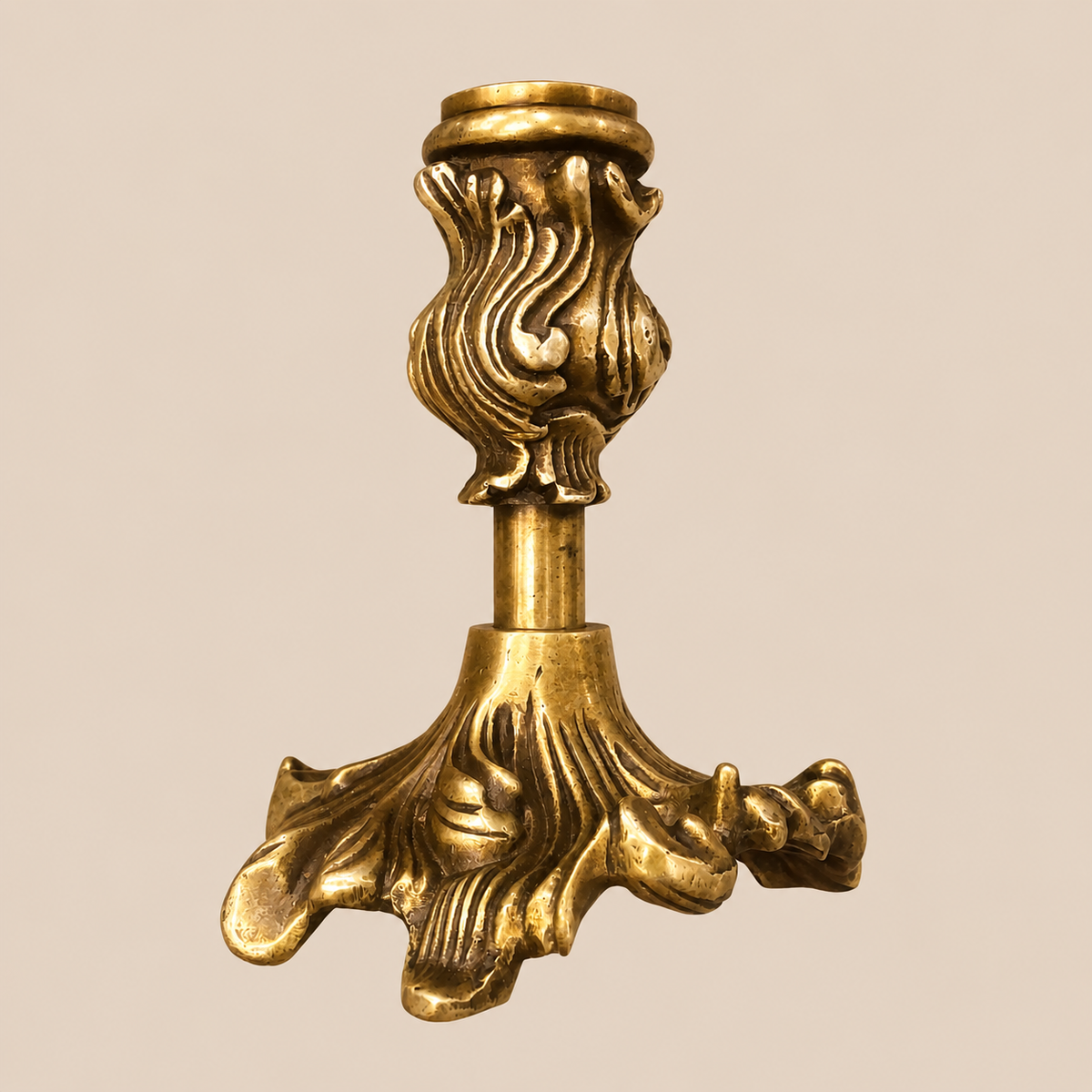 An ornate antique-style brass candle holder with a fluted acanthus leaf base design and a matching decorative stem, shown against a solid beige background.