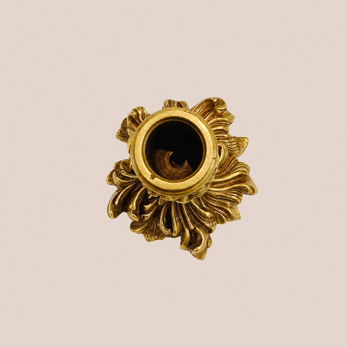 An ornate gold brass candle holder with a decorative floral design, shown from a top-down view on a solid light beige background.