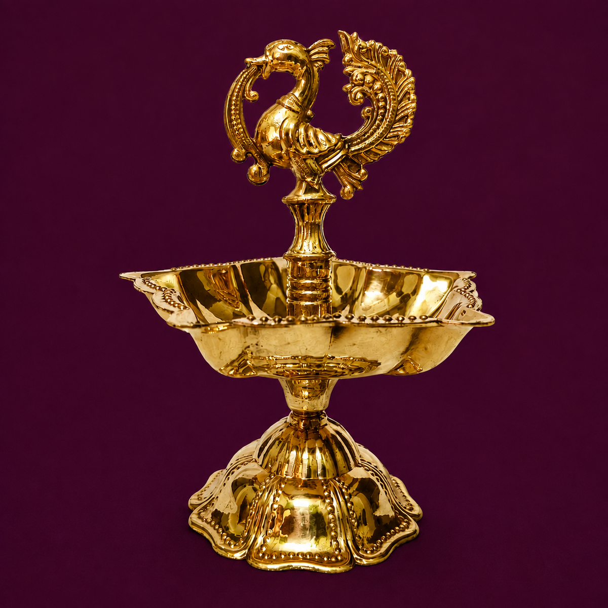 A polished gold-toned brass oil lamp with a decorative peacock finial on top, set against a solid deep purple background.