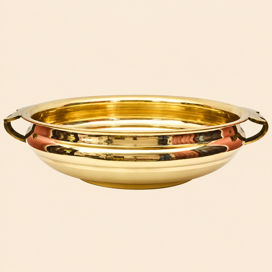 A polished golden plain brass Urli bowl with side handles, shown on a warm beige background. The bowl is reflective and has a warm golden hue under soft lighting.