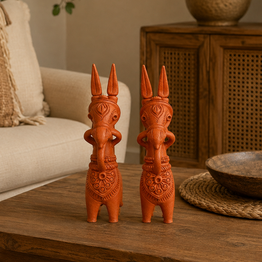 A pair of terracotta Bankura horse figurines resembling, displayed on a wooden table in a cozy living room setting.