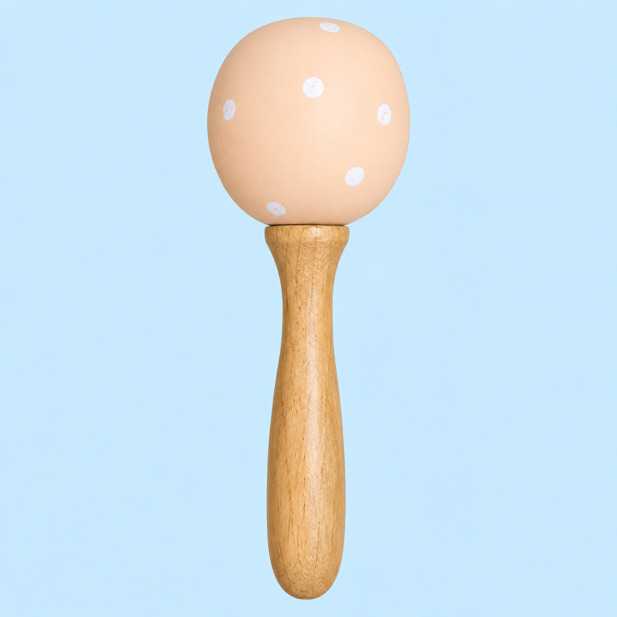 A wooden baby rattle with a round peach-colored painted head decorated with white polka dots and a natural light wood handle, shown against a solid light blue background.