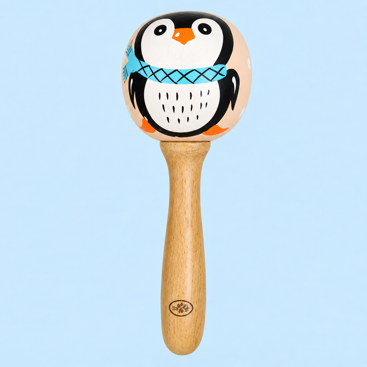 A wooden baby rattle with a penguin design on the top ball. The rattle features a natural wood handle and a spherical head decorated with a hand-painted penguin wearing a blue patterned scarf, set against a solid light blue background.