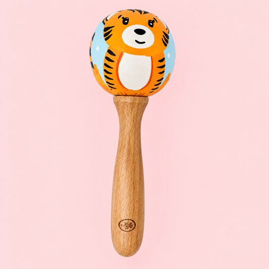 A wooden baby rattle with a hand-painted tiger face on the top ball, set against a solid light pink background.