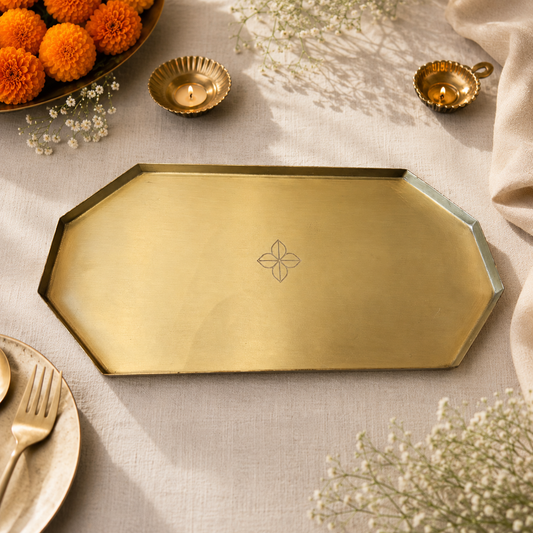 An octagonal brass serving tray with a subtle floral engraving in the center, styled on a beige linen tablecloth with decorative flowers, candles, and a plate.