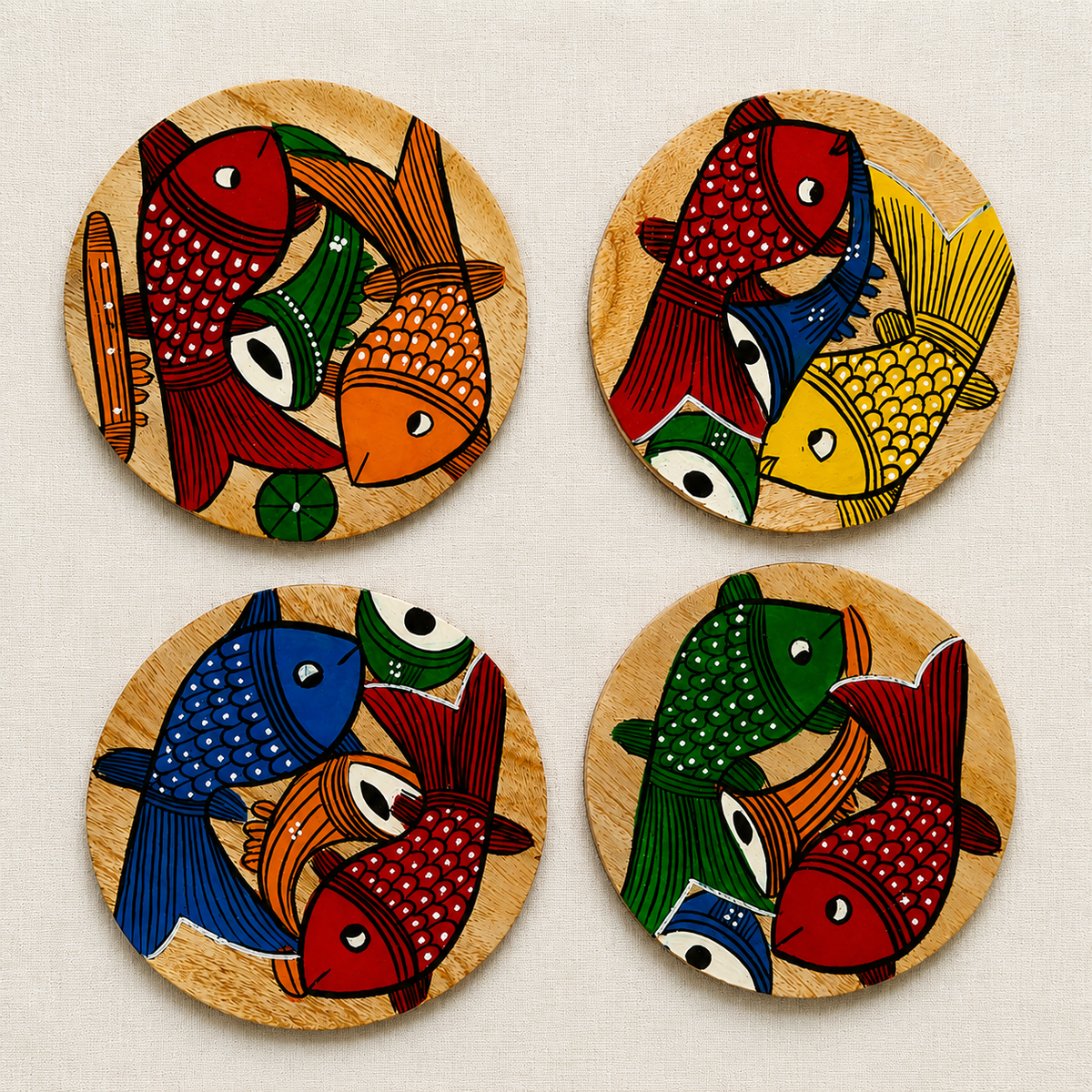 Four round wooden coasters featuring colorful hand-painted Patachitra fish designs in red, blue, green, orange, and yellow, arranged in a 2x2 grid on a light beige textured background.