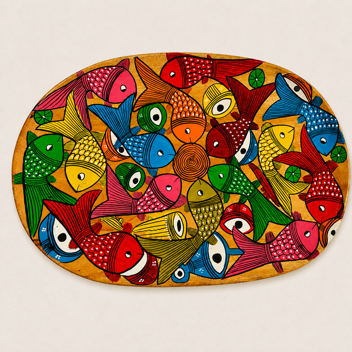 An oval decorative wooden serving tray featuring a dense, colorful Patachitra folk-art style illustration of numerous fish in red, blue, green, yellow, pink, and orange on a warm tan background, photographed flat against a light neutral backdrop.