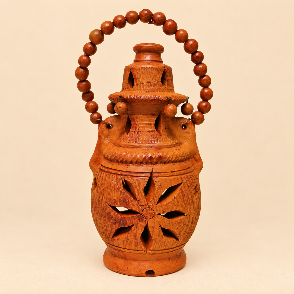 A carved Terracotta decorative lantern with a beaded handle, photographed against a plain beige studio background.