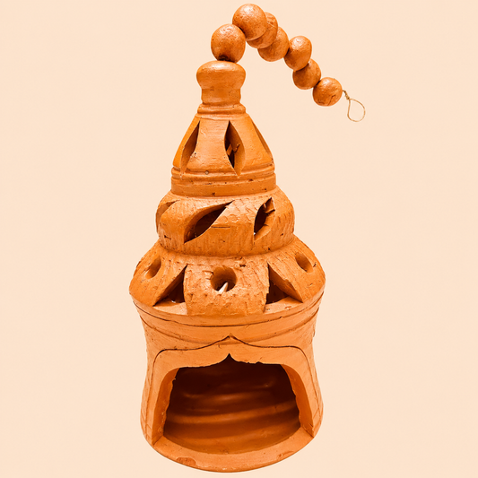An orange-brown terracotta hanging lamp with carved cutouts and a beaded hanging loop, shown against a solid pale peach background.