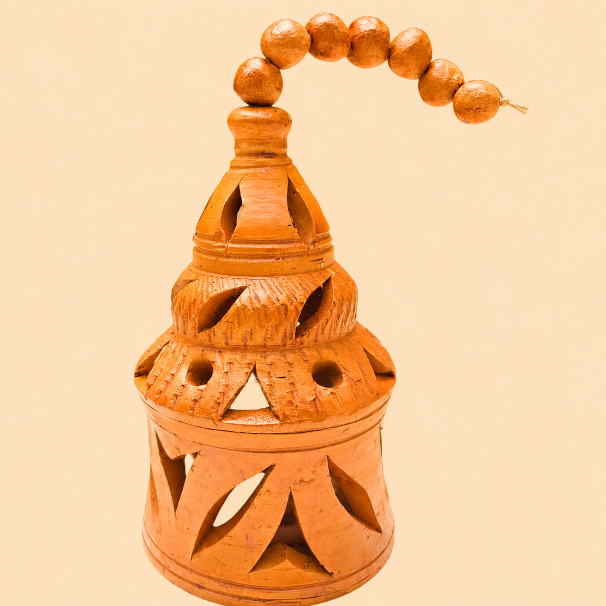 An orange-brown terracotta hanging lamp with carved cutouts and a beaded hanging loop, shown against a solid pale peach background.