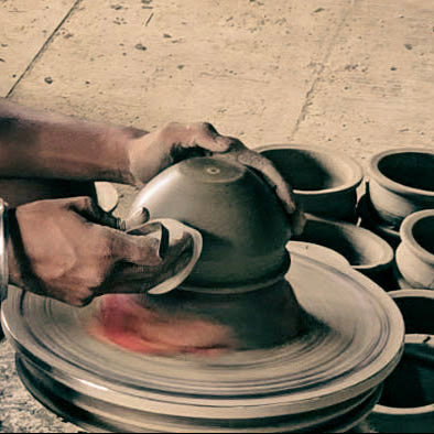 A potter's wheel scene showing a person shaping a clay bowl on a spinning wheel, with many finished clay bowls arranged in the background.